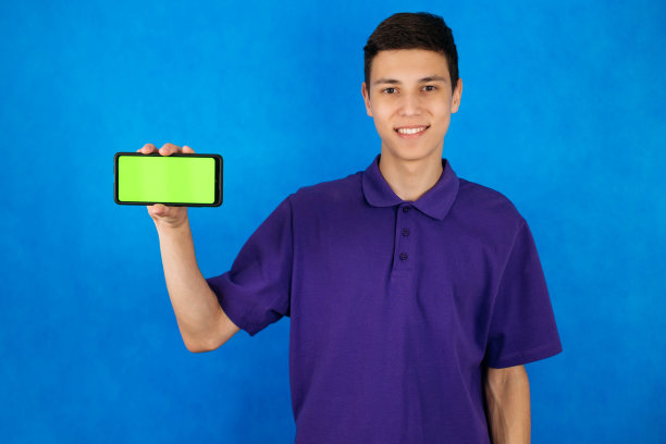 一个少年的特写肖像，蓝色背景，手里拿着一个绿色屏幕的智能手机，复制空间图片下载