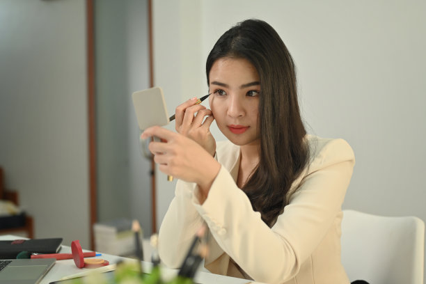 年轻迷人的女商人穿着时髦的西装，在工作场所化妆，画眼线。图片下载