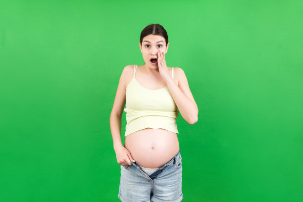 孕妇在解开的牛仔裤显示她裸露的腹部在彩色背景与复制空间图片下载