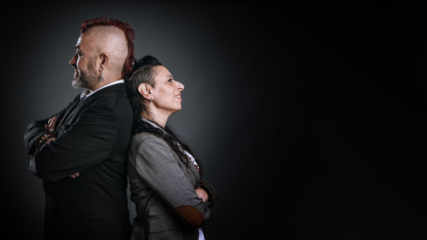 一男一女穿着朋克风格和优雅的连衣裙，背对着对方在工作室里摆姿势。图片下载