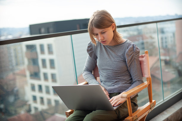年轻女孩坐在导演的椅子上使用笔记本电脑，而在阳台上图片下载