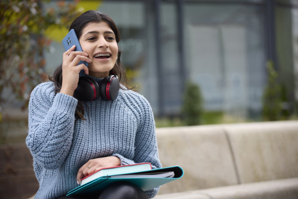女大学生戴着无线耳机在教学楼外打手机图片下载