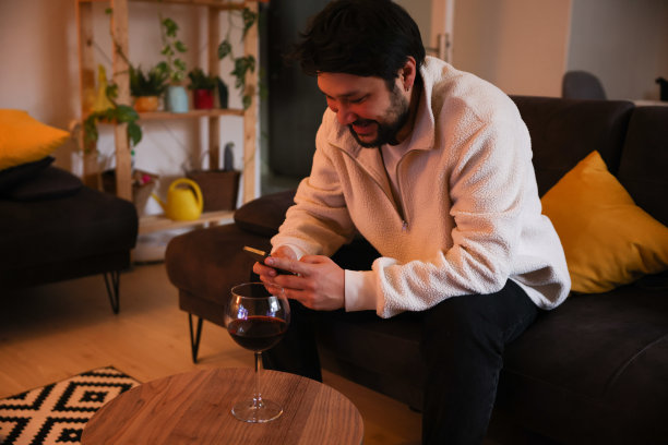 年轻人在家里一边喝红酒一边用智能手机图片下载