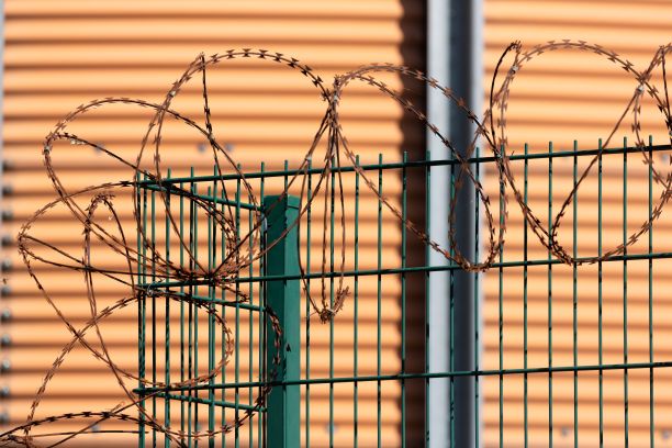 有带刺铁丝的栅栏背景是圆形的橙色筒仓墙。图片下载