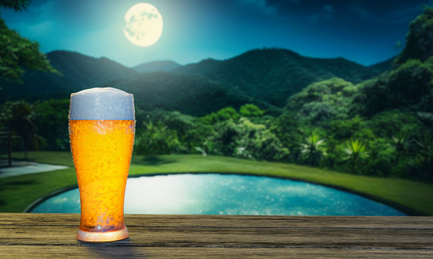 生啤，在木桌面上的一个有水滴的高脚杯里起泡。背景森林和山与满月。草坪上的池塘在森林的开阔地带。浪漫的酒精饮料。三维渲染图片下载