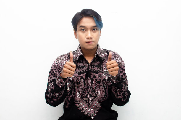 一个穿着印度尼西亚蜡染衬衫的年轻亚洲男子竖起大拇指表示赞扬和认可。图片下载