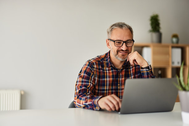 微笑的老年商人在家庭办公室的笔记本电脑前工作。图片下载