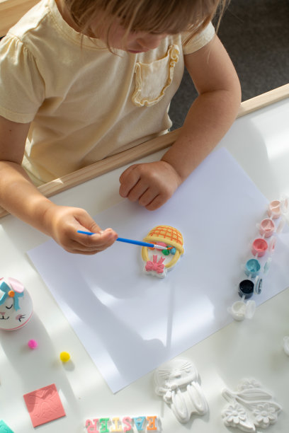 一个可爱的小女孩正坐在桌子旁做复活节工艺品，给复活节小雕像上色。创造力和爱好。图片下载