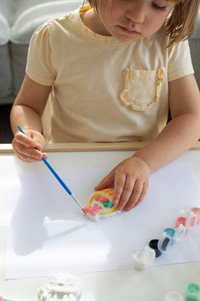 一个可爱的小女孩正坐在桌子旁做复活节工艺品，给复活节小雕像上色。创造力和爱好。图片下载