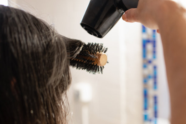 女人的手拿着梳子，同时使用吹风机在浴室镜子前梳头图片下载