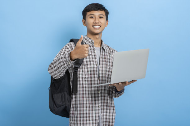 年轻的亚洲大学生携带书籍和背包手提电脑积极显示大拇指孤立在蓝色背景图片下载