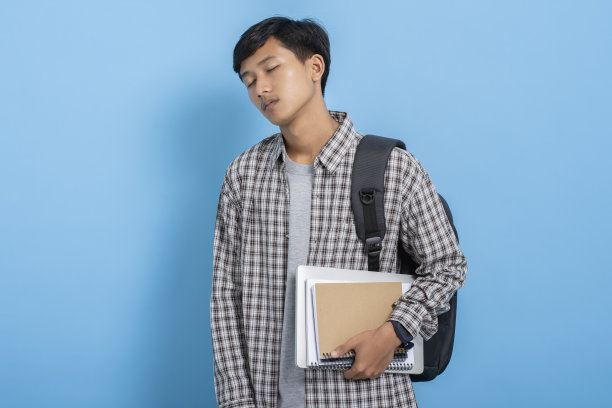年轻的亚洲大学生背着书和背包，在蓝色的背景下感到困倦和疲惫图片下载
