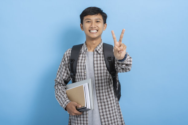 年轻的亚洲大学生携带书籍和背包微笑显示数字手势与手指孤立在蓝色背景图片下载