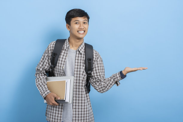 年轻的亚洲大学生背着背包显示目前的产品和广告，双手孤立在蓝色背景图片下载