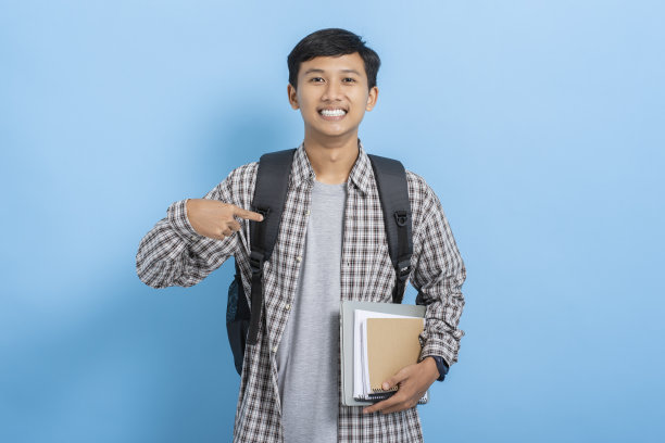 年轻的亚洲大学生背着书和背包自信地指着自己孤立的蓝色背景图片下载