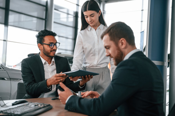 一名妇女正在分发文件。三个人在汽车陈列室里一起工作图片下载