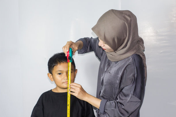 戴头巾的年轻女子在测量一个男孩的身体图片下载