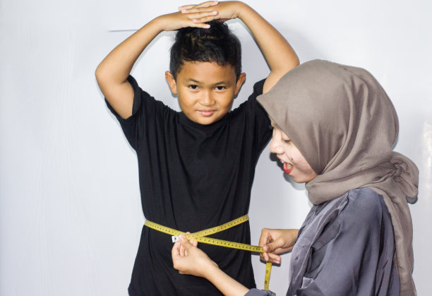 戴头巾的年轻女子在测量一个男孩的身体图片下载