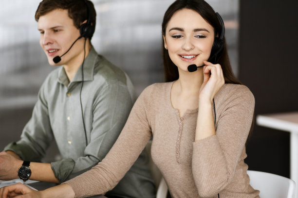 两名戴着耳机的年轻人坐在办公室的办公桌前与客户交谈。关注女性。呼叫中心接线员在工作图片下载