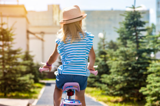 小女孩在粉红色的帽子骑自行车在夏季公园，户外的后视图。小金发孩子喜欢骑着小自行车在外面，夏天的时候，在阳光明媚的日子。童年的概念。复制广告文字空间图片下载