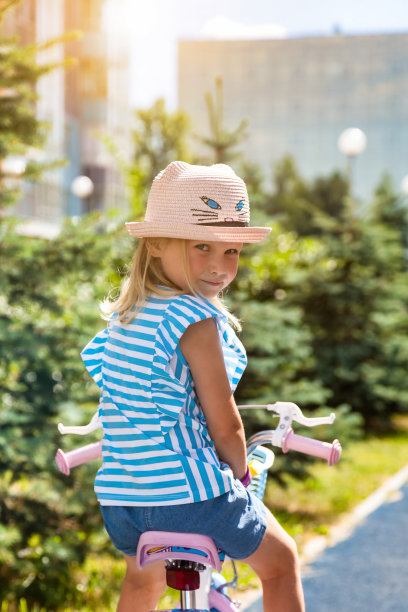 戴着粉色帽子的小女孩坐在户外的自行车上，转过身看着镜头。可爱的金发孩子喜欢骑小自行车，夏天。童年休闲活动概念。本空间图片下载