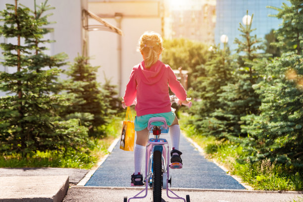 孩子骑自行车在夏天的城市公园，户外的后视图。可爱的小金发女孩喜欢骑小自行车的路径，夏天，在阳光明媚的日子。童年的概念。复制广告文字空间图片下载