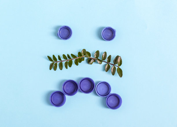 深蓝色的塑料瓶盖被排列成一个带眼睛的脸的形状，一个悲伤的微笑。图片下载