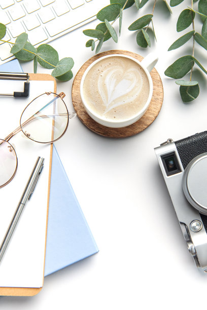 现代白色办公桌桌上配有笔记本电脑、相机、笔记本等用品。图片下载