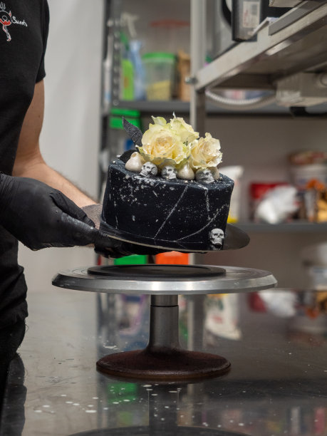 厨师浇上黑色喷枪画的糖霜蛋糕顶部两个真正的玫瑰银喷和可食用的巧克力骷髅图片下载