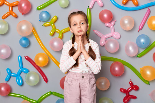 可爱的恳求小女孩的肖像，辫子，穿着休闲服装，在灰色背景上与气球隔离，保持手掌祈祷的姿势，请求原谅。图片下载