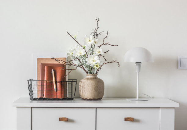 极简风格的客厅内部。插花，台灯，白色五斗橱上放着杂志的金属篮子图片下载