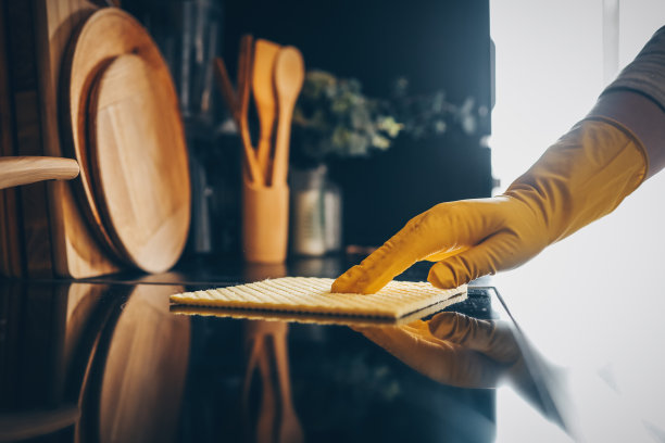 女性戴着黄色橡胶手套的手用海绵清洁厨房橱柜的特写镜头。图片下载