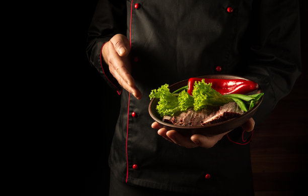 厨师手里拿着一盘切好的牛肉和蔬菜。在深色背景上烹饪的概念。欧洲菜图片下载