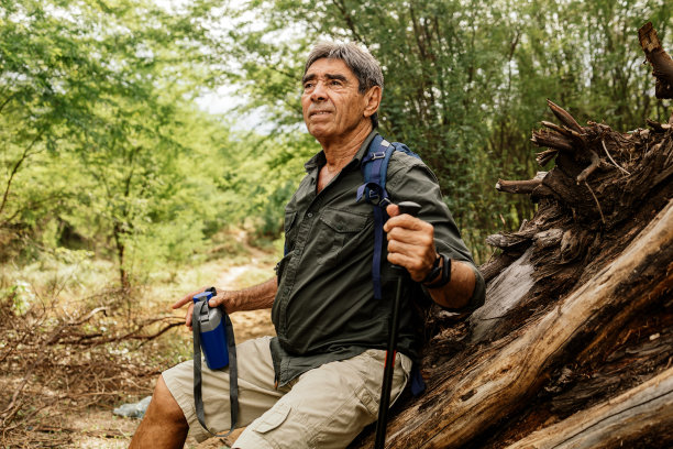 背着背包和登山杆的老人在树林里徒步旅行，欣赏风景或停下来喘口气。图片下载