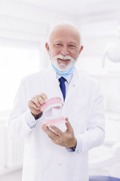 老年牙医拿着塑料下颌模型图片下载