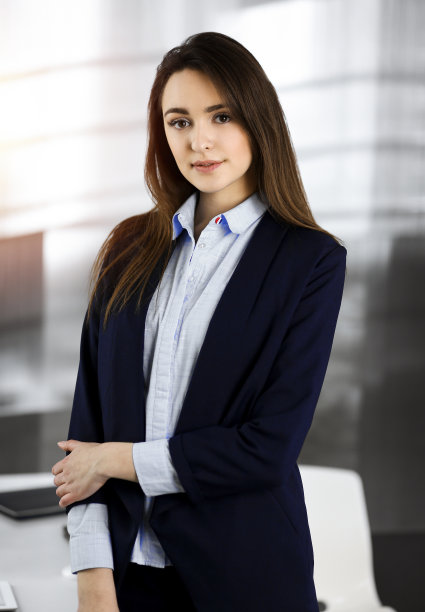 穿着蓝色夹克的聪明的年轻女商人站在她的工作场所。一个专家的肖像在阳光明媚的办公室图片下载