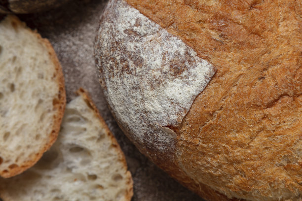 面包拼盘有三种面包，荞麦面包，小麦面包和黑麦面包。面包裹在亚麻毛巾里，放在咖啡色的深色背景上。旁边放着几片面包、一碗酸奶油和一根葱。图片下载