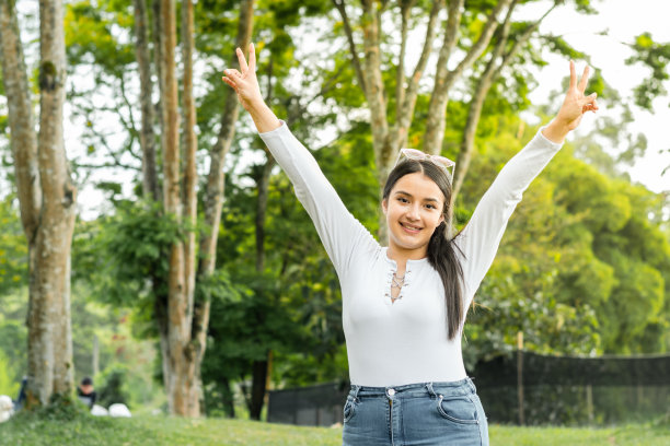 美丽的拉丁女孩的肖像，举起她的双手在胜利，而在公园散步。图片下载