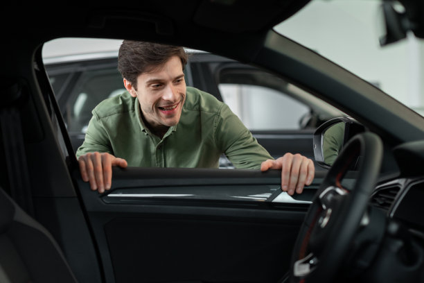 英俊的年轻人通过窗户看在新车，检查它之前购买在现代经销商商店图片下载