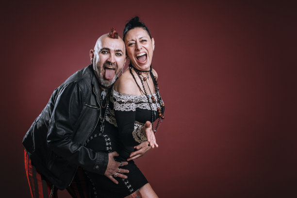 朋克风格的男人和女人pose在工作室与欢快的表情在红色背景图片下载