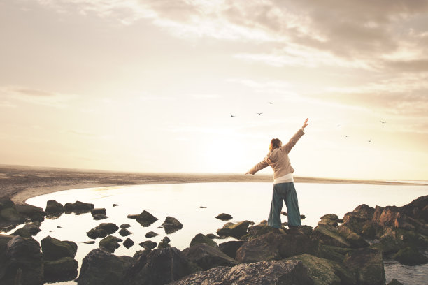 一名女子张开双臂在壮观的海洋全景前冥想图片下载