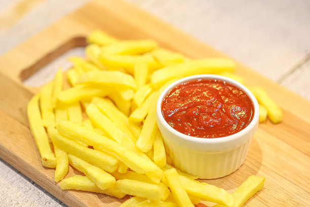 炸薯条铺在木板上，番茄酱放在木桌上的碟子里。特写照片。图片下载