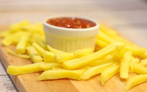 炸薯条铺在木板上，番茄酱放在木桌上的碟子里。特写照片。图片下载