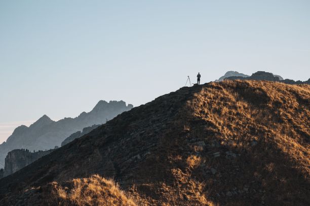 一名男子站在长满草的山顶上，用三脚架上的相机拍照图片下载