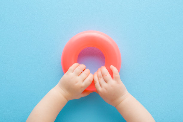 宝宝的手在浅蓝色的桌子背景上玩粉红色的塑料戒指。柔和的颜色。特写镜头。视角镜头。适合小孩子发展的玩具。自顶向下视图。图片下载