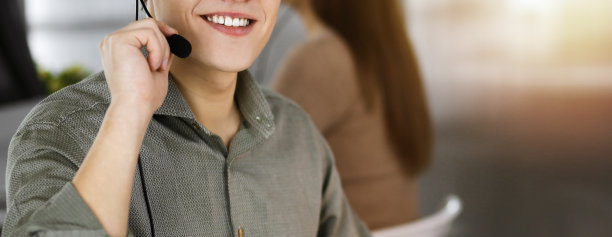 年轻男子戴着耳机正在和客户交谈，而坐在现代阳光充足的办公室。呼叫中心接线员在工作图片下载