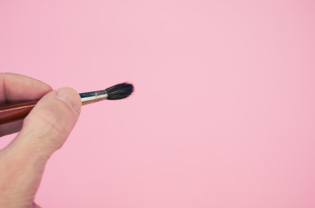一个人拿着画笔靠近粉红色背景的特写镜头图片下载