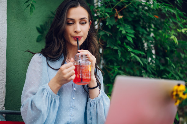 一名女子坐在街边咖啡馆边喝冷饮边用笔记本电脑图片下载