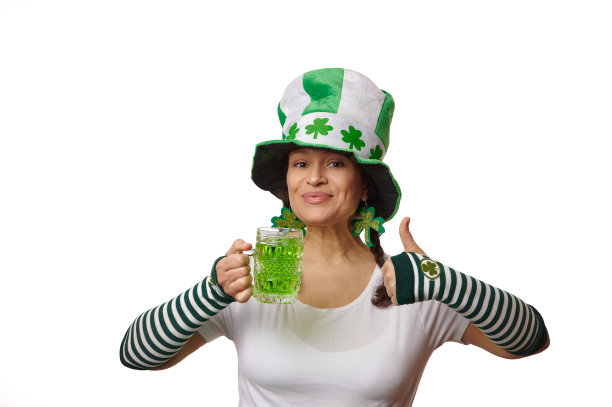 女人戴着有三叶草叶子的妖精帽子，拇指朝上，拿着白底绿啤酒的杯子图片下载