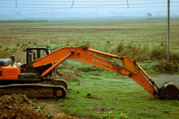 一辆反铲装载机、挖掘机、挖掘机，绿色农田上的重型工业车辆。图片下载